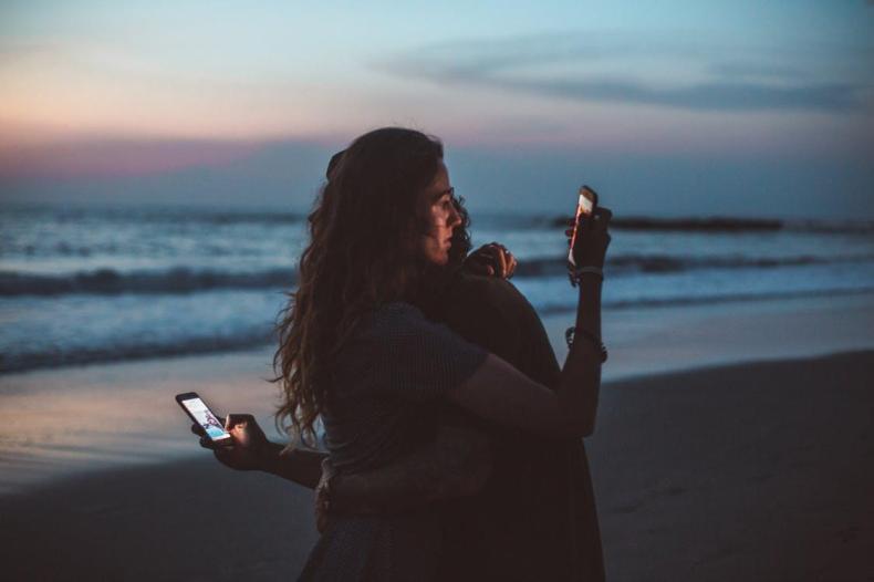 Free Couple hugging and using smartphone near sea on sunset Stock Photo