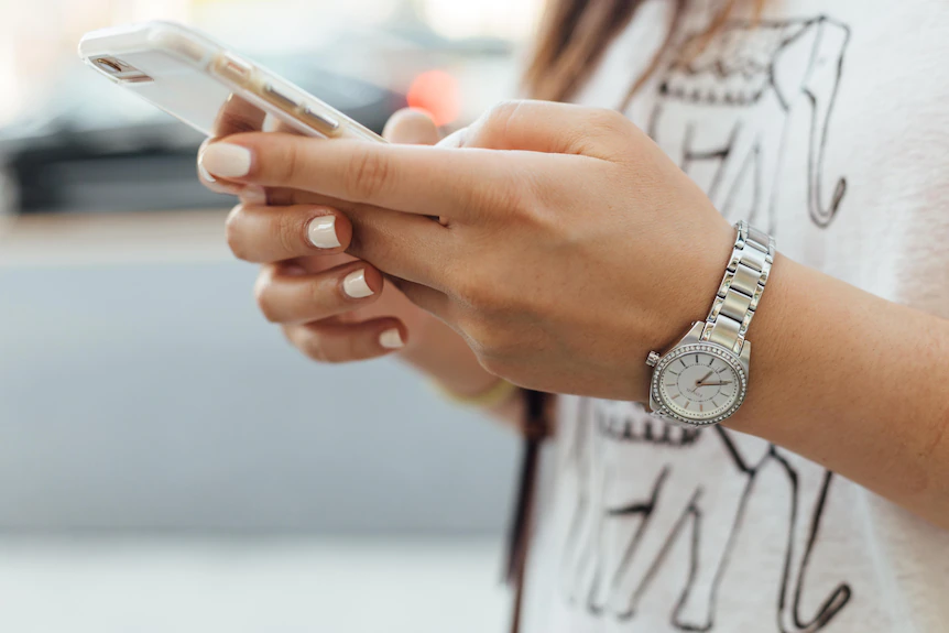 Phone in hands with nice watch and pastel nail polish. 