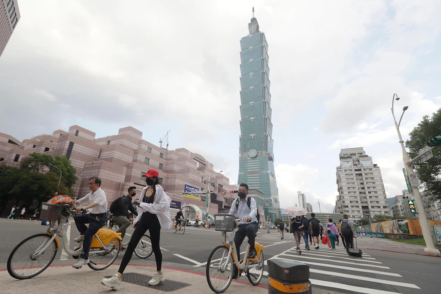 People cross a street with an iconic Taipei building in the background 