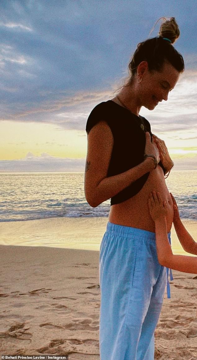 Special moment: The former Victoria's Secret Angel additionally shared a photo of one of her daughters gently resting their hands on her baby bump as they enjoyed a beach day