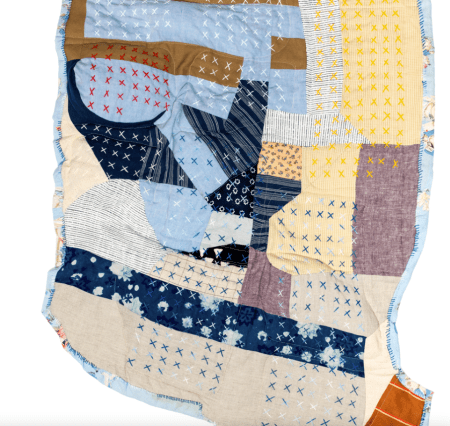 Shows an asymmetrical quilt sewn with different colored fabrics of different textures and weaves.