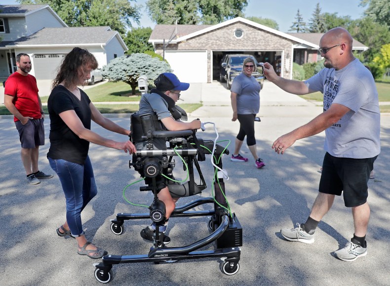 Physical therapist Jody Streeter, Johannes Jerman, right, Lisa Jerman, center right, and a neighbor walk with Mason Jerman as he uses a Trexo Robotics Gait Training System during a physical therapy session with on Tuesday, July 12, 2022 in North Find du Lac, Wis. Mason suffered brain damage in 2018 from complications at the hospital while getting treated for pneumonia and is learning to walk and talk again.