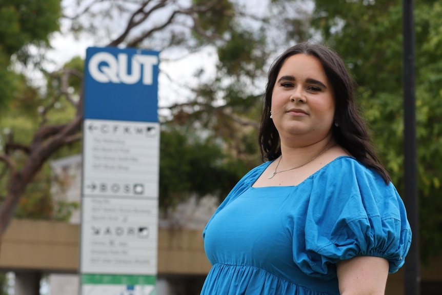 QUT Student Guild president Zoe Davidson with trees and a university sign behind her