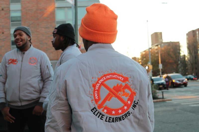 Three men stand outside wearing hats and matching grey jackets.