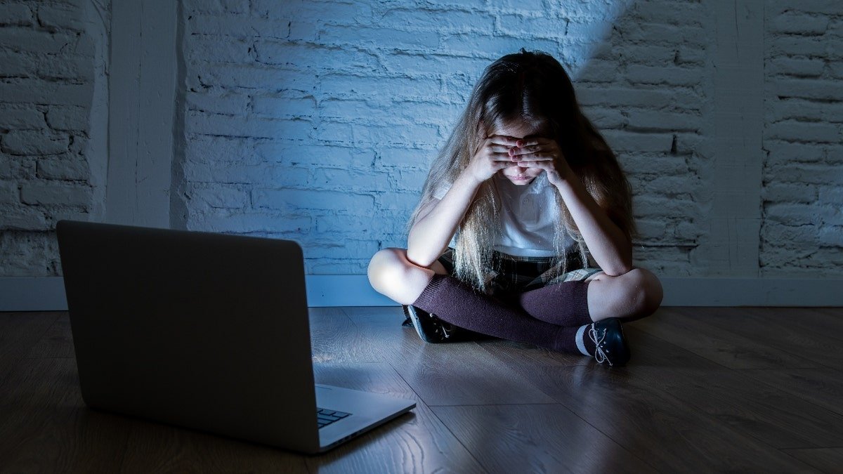 A girl looks scared in front of a laptop