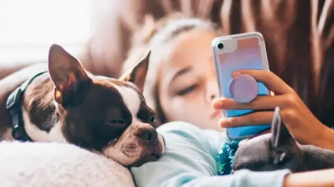 Getty Images A stock photo of a girl and her dog looking at a phone on a couch