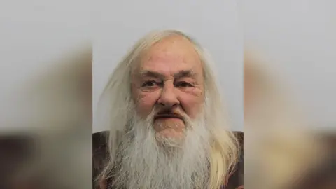 Met Police A custody image of David Cheneler. He has long white hair and a white beard. 