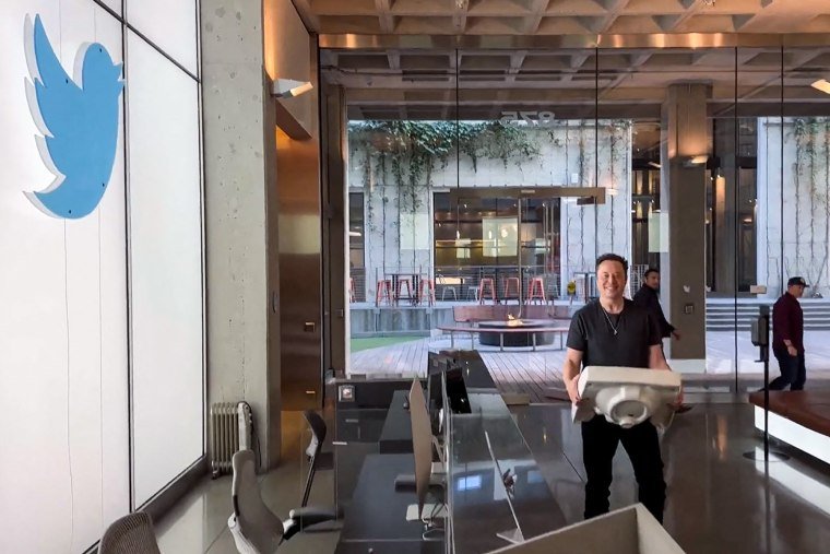 Elon Musk walks while holding a sink inside of an office