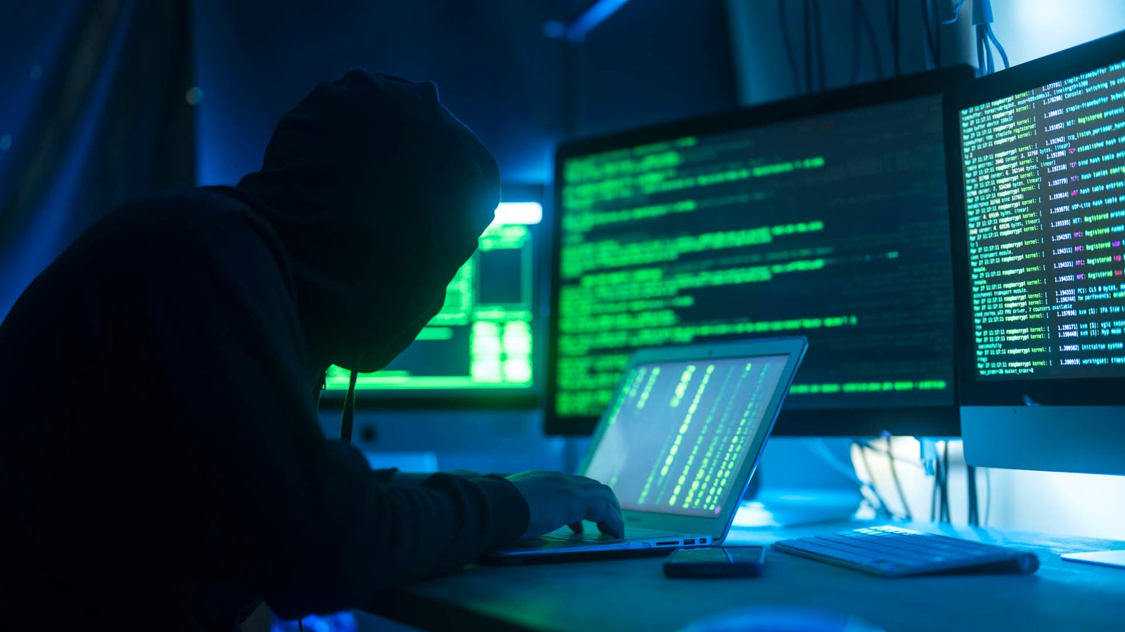 A stylised photograph of a person acting as a hacker, break into servers and infecting them with a virus, as show by computer monitors displaying green text and codes Their System with a Virus