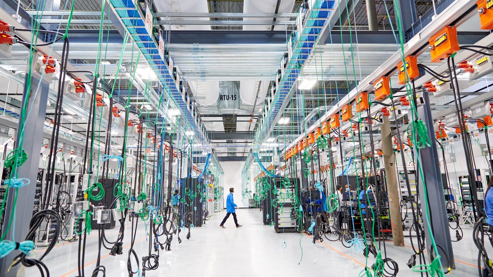 A photo of a large computer centre, showing clean white floors and many cables hanging from the ceiling