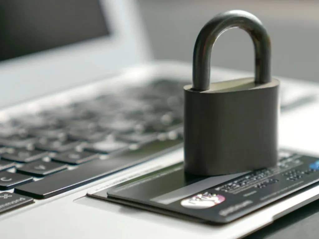 A lock sits on top of a credit card, on top of a laptop.