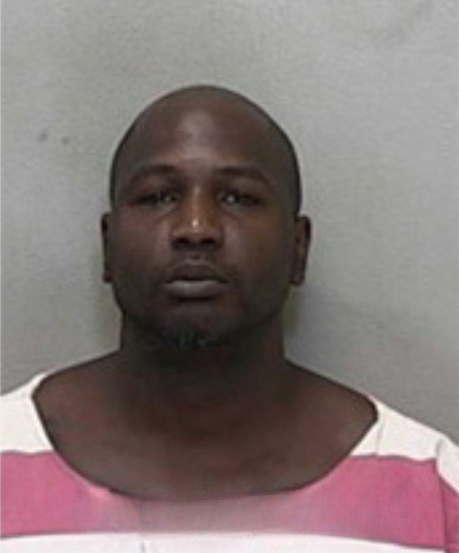 Mugshot of a bald man with a trimmed beard, wearing a red-and-white striped jail uniform.