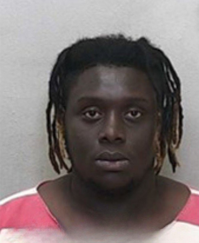 Mugshot of a man with medium-length dreadlocks, wearing a red-and-white striped jail uniform.
