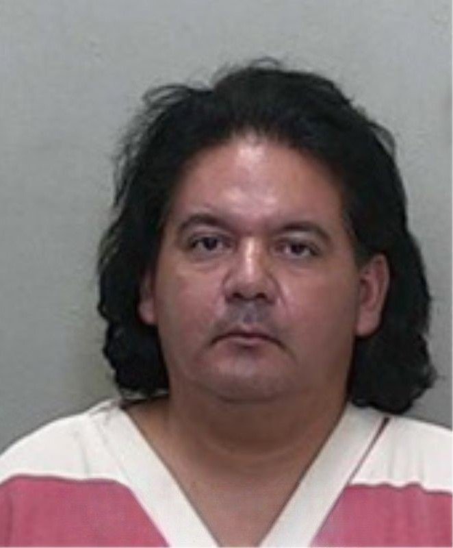 Mugshot of a man with long dark hair, wearing a red-and-white striped jail uniform.