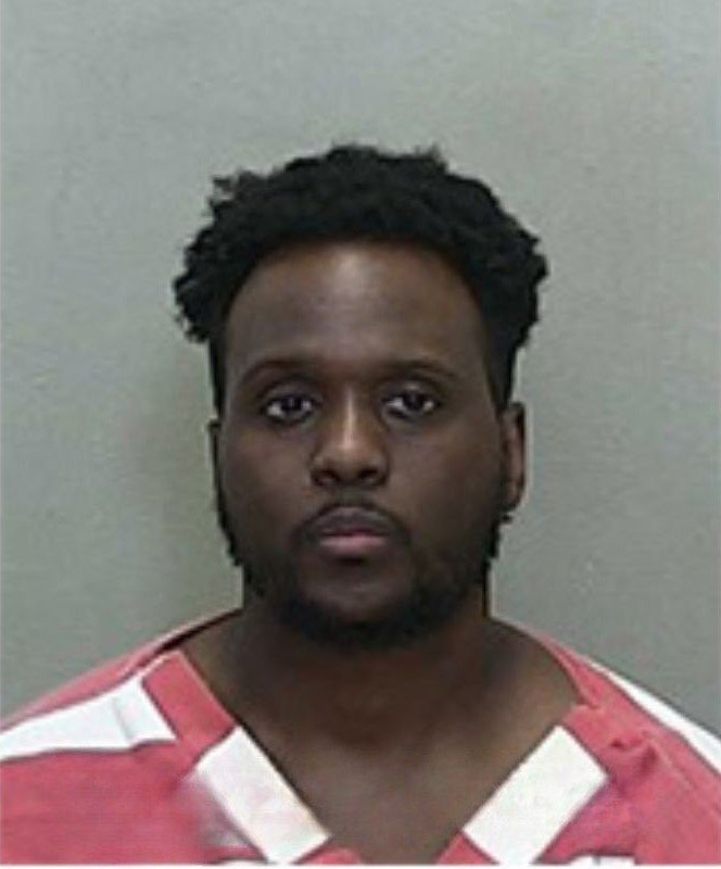 Mugshot of a man with short hair and a goatee, wearing a red-and-white striped jail uniform.