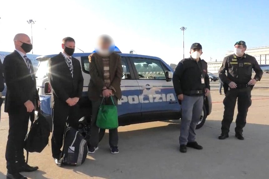 A group of masked men stand in front of a car marked Polizia.