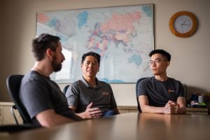 Three men sit in a conference room, discussing.