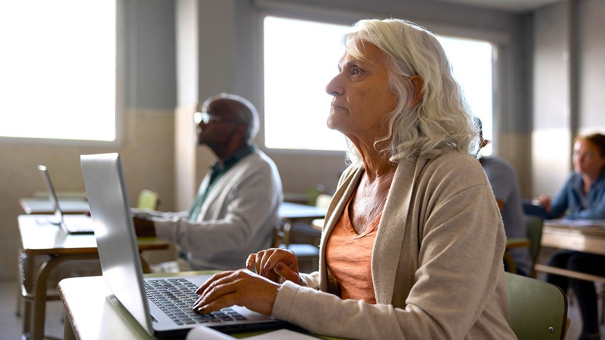 senior woman types on laptop in classroom